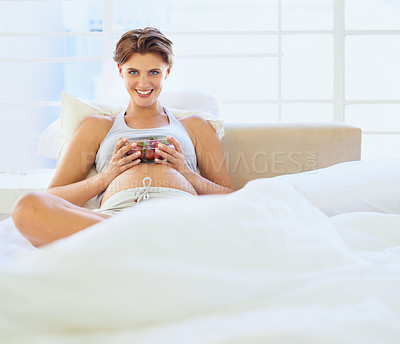 Buy stock photo A young pregnant woman sitting in bed holding a bowl of strawberries