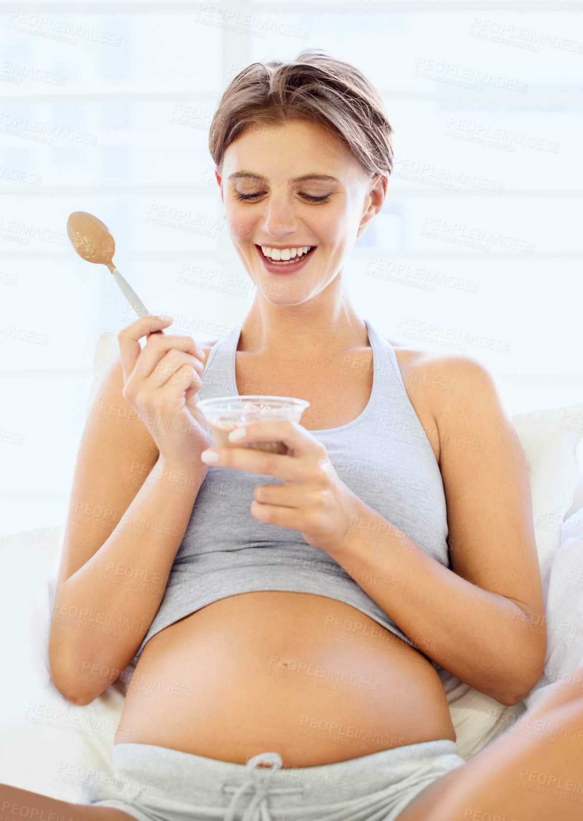 Buy stock photo A happy young pregnant woman eating a small bowl of pudding