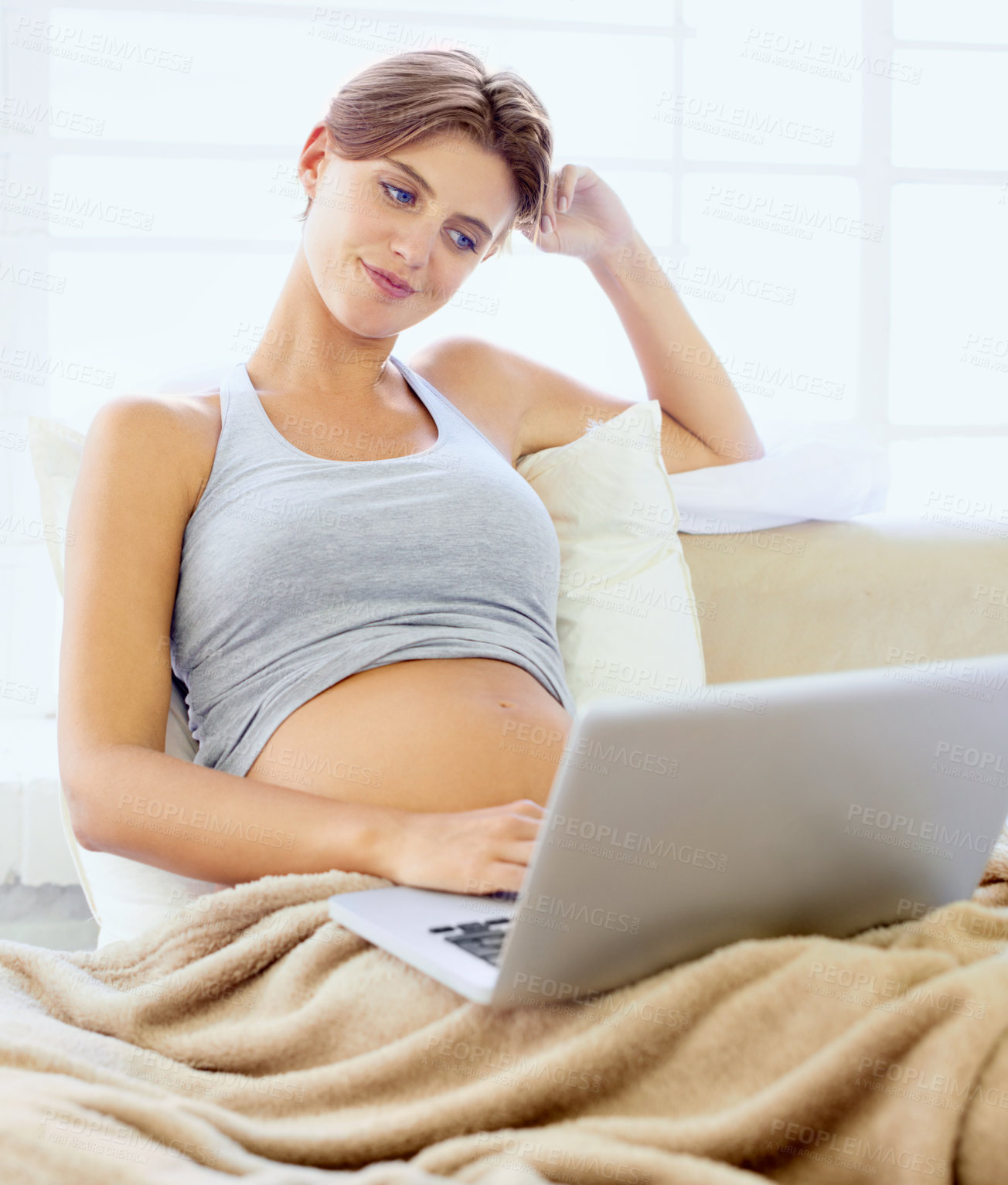 Buy stock photo A lovely young pregnant woman sitting in bed with her laptop