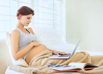 Buy stock photo A young pregnant woman sitting in bed and working on her laptop