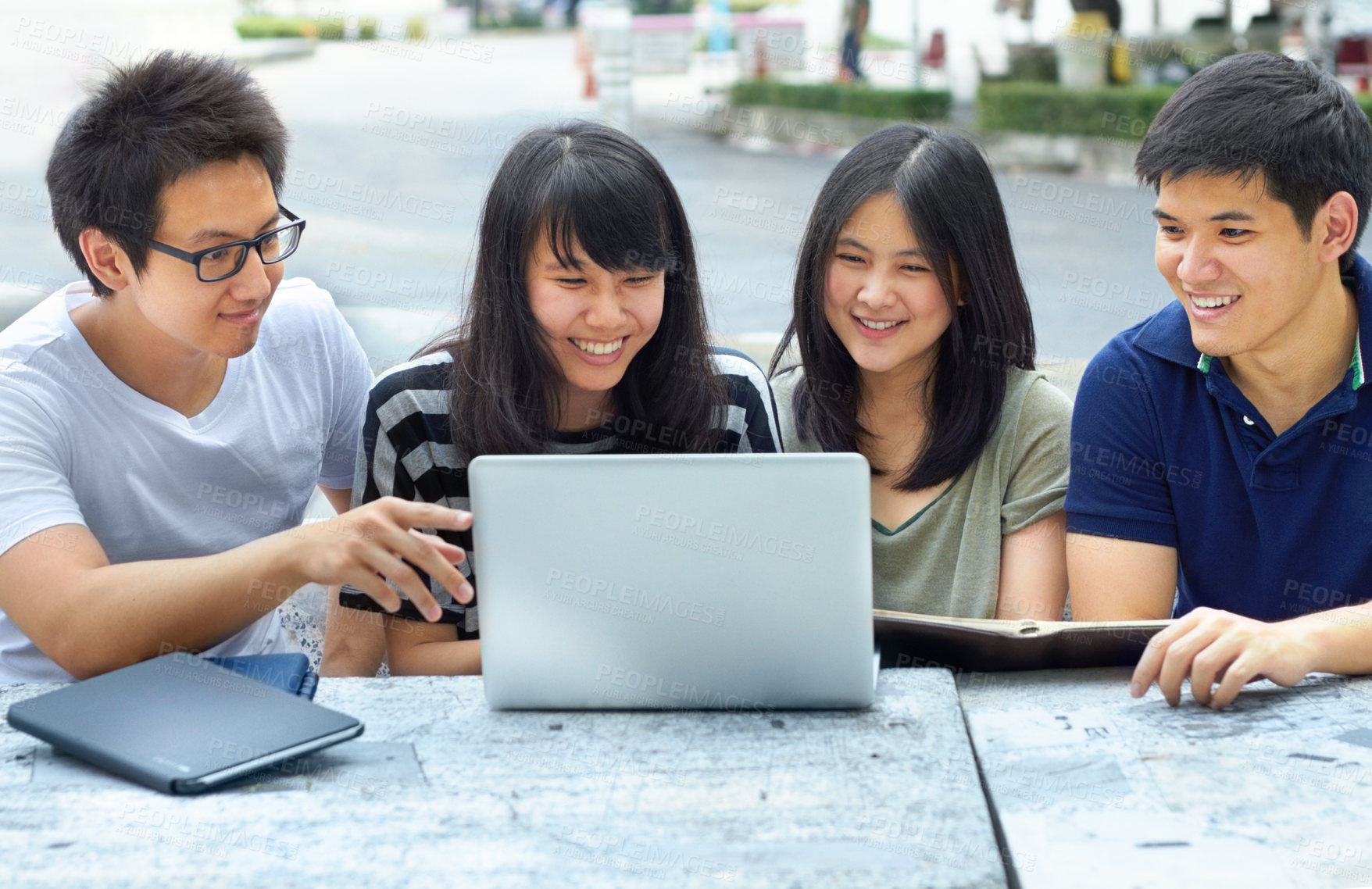 Buy stock photo Four young students sharing a laptop outside