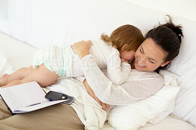 Buy stock photo A young mother lying in bed and giving her toddler a hug with an open notebook lying on her back