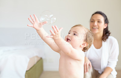 Buy stock photo An adorable baby girl reaching for a bubble with her mother smiling in the background - copyspace