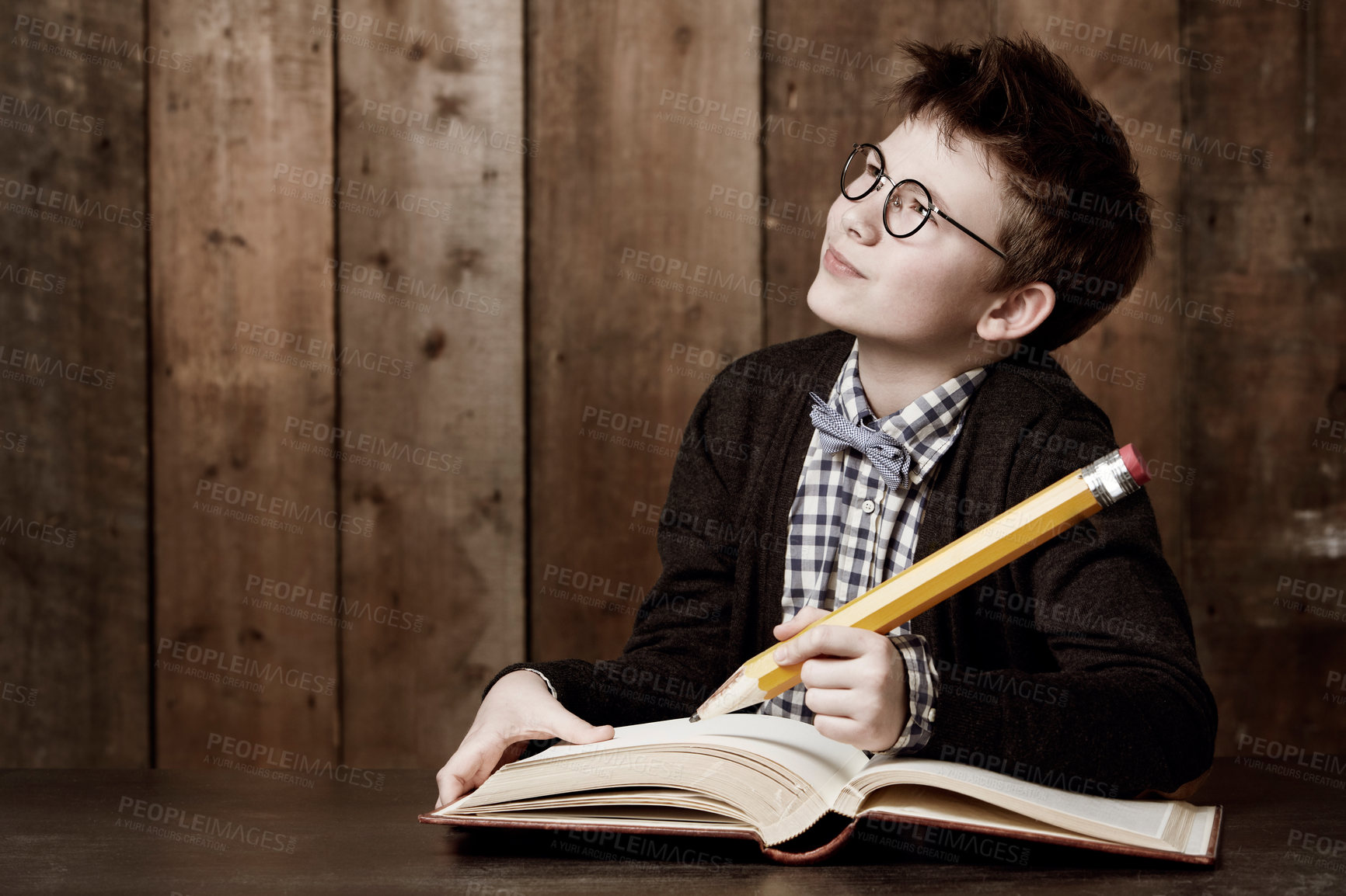 Buy stock photo Young boy wearing glasses and doing his homework with an enormous pencil