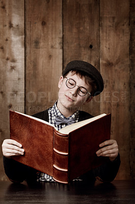Buy stock photo Young boy in retro clothing wearing spectacles reading a massive book thooughtfully
