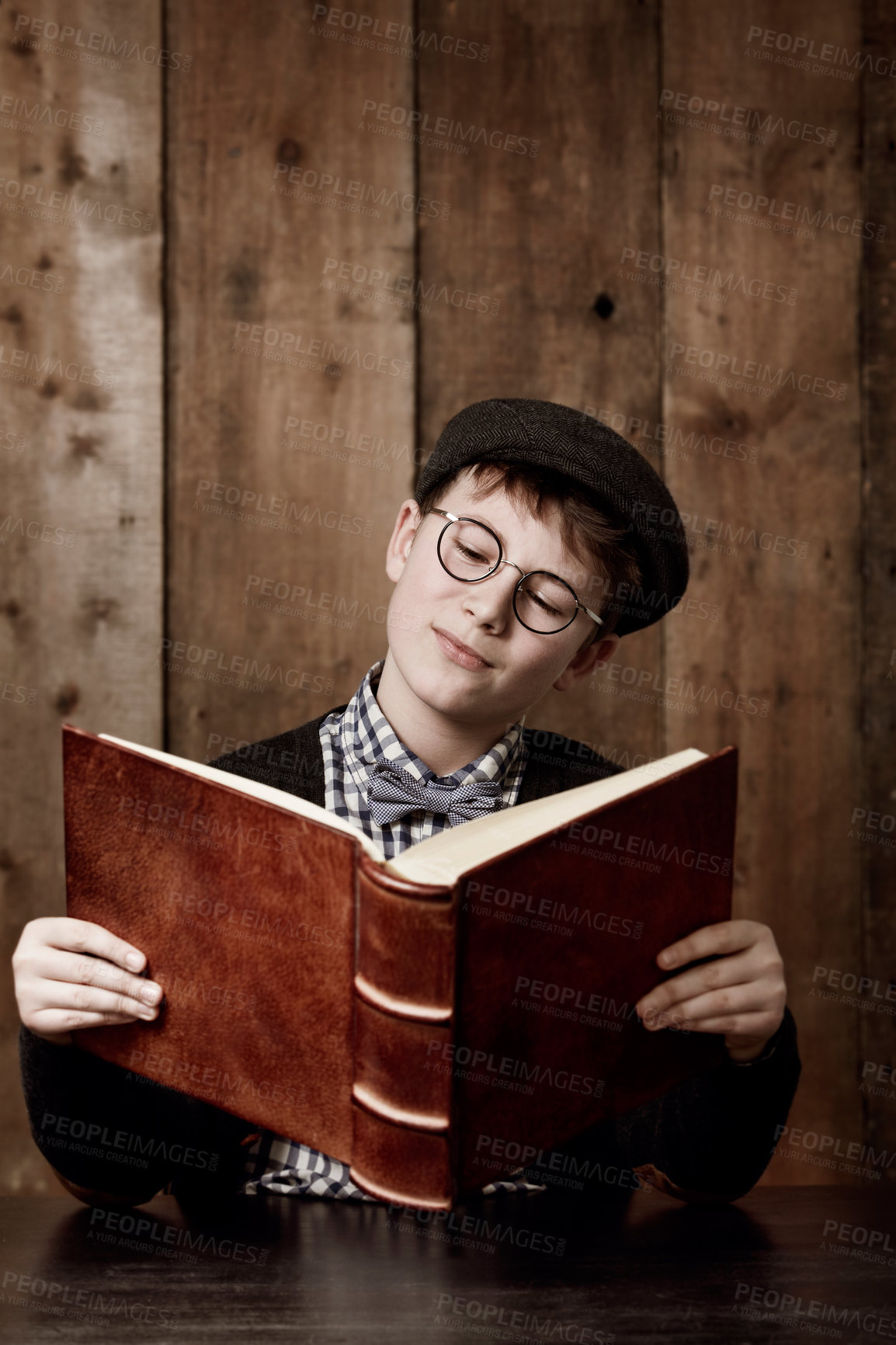 Buy stock photo Young boy in retro clothing wearing spectacles reading a massive book thooughtfully