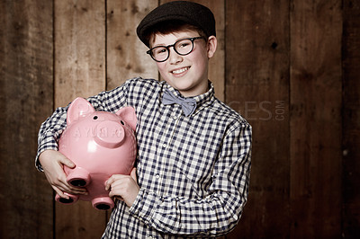 Buy stock photo Young child, piggy bank or smile in portrait by wooden background, money saving or growth in youth in retro fashion. Boy, smile and face for coin banking and safe for bills with glasses by backdrop