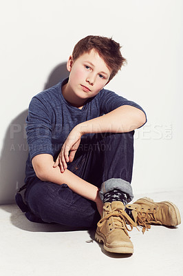 Buy stock photo Serious, teenager and portrait of boy with fashion sitting in white background of studio. Cool, style and kid with confidence and pride in trendy outfit or clothes with boots and jeans on backdrop