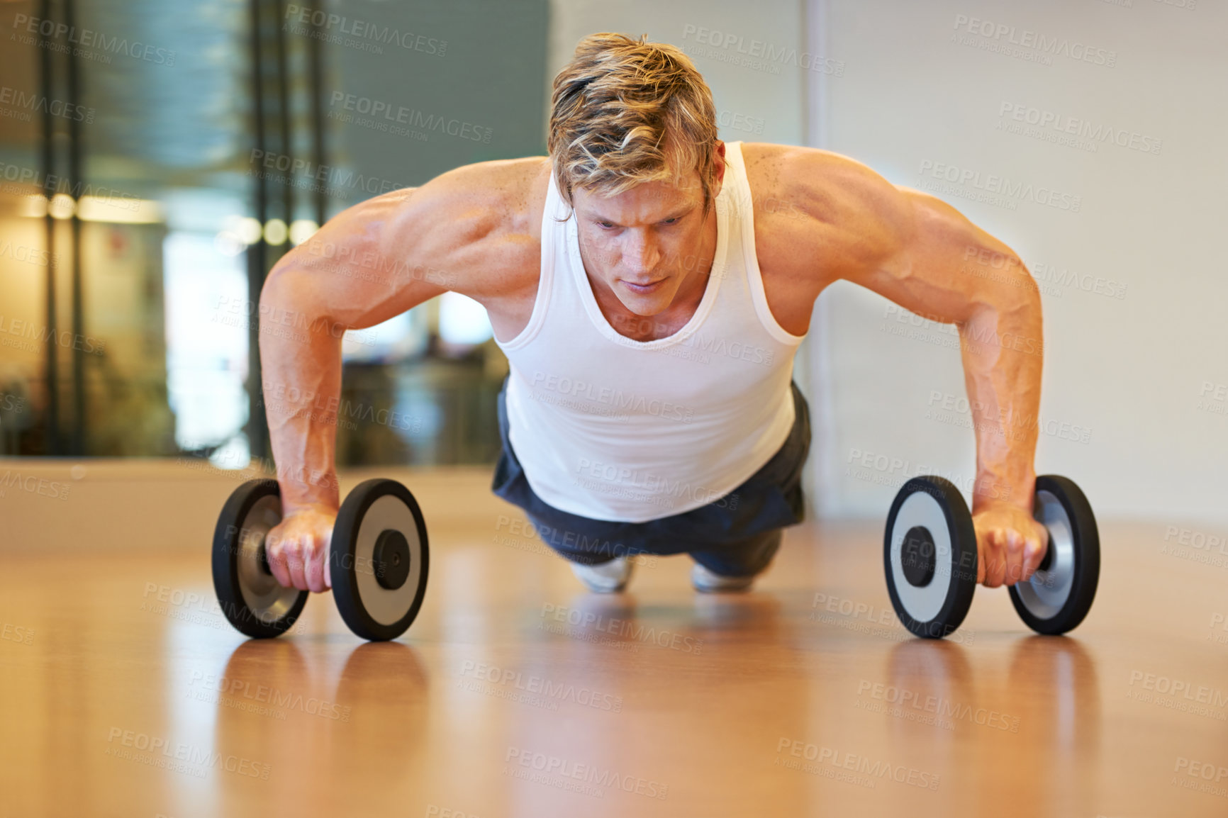 Buy stock photo Fit young man doing push ups in a health club using dumbbells