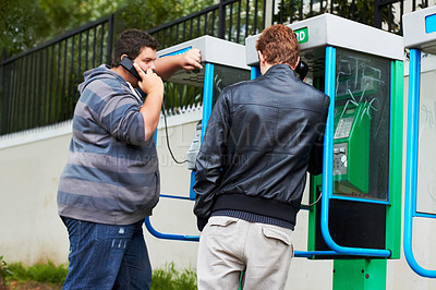 Buy stock photo Two young men making phone calls from public pay-phone booths
