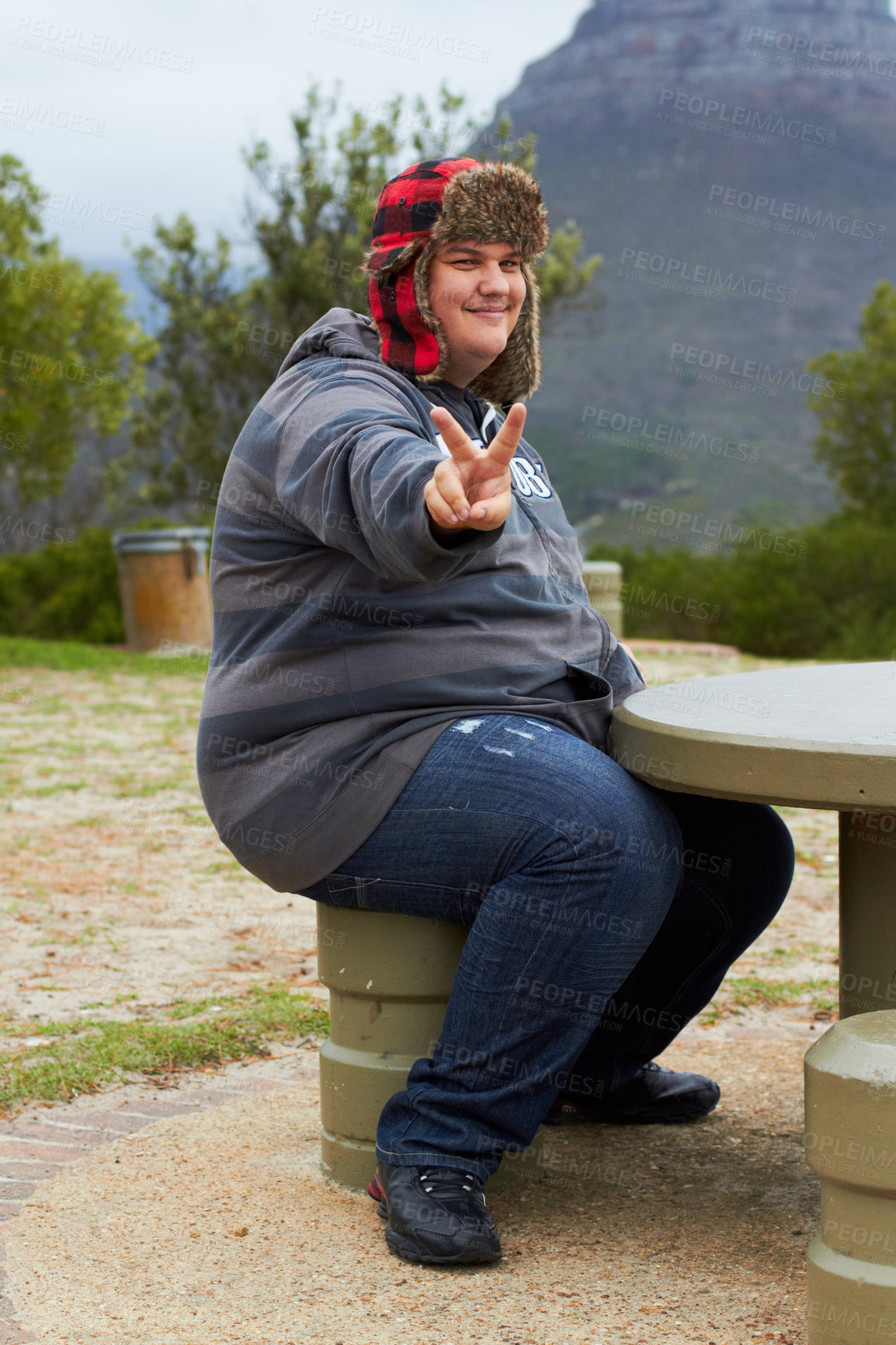 Buy stock photo An obese young man sitting outside at a picnic table showing a peace-sign