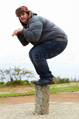 Buy stock photo An overweight young man in winter wear balancing playfully on a post