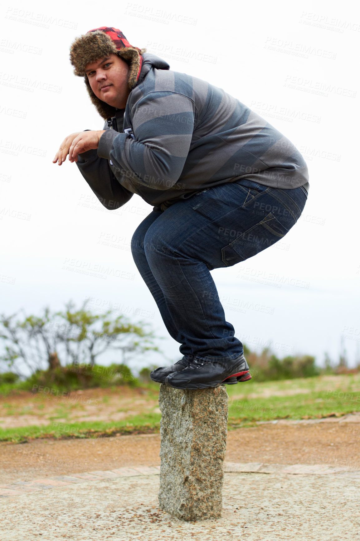 Buy stock photo An overweight young man in winter wear balancing playfully on a post