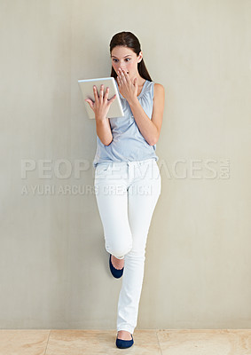 Buy stock photo Woman, tablet and shocked on social media, news or gossip leaning against a wall at home. Surprised female person, brunette or freelancer gasping on technology for notification, alert or information