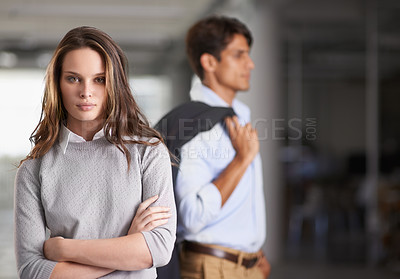 Buy stock photo A confident young businesswoman standing with arms folded and her colleague in the background