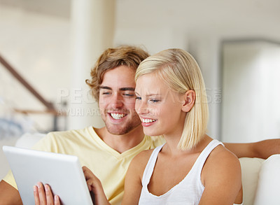 Buy stock photo A happy young couple using a tablet together in their lounge