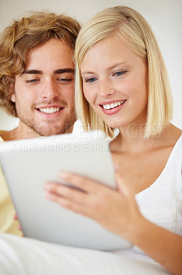 Buy stock photo A young couple browsing the internet on their tablet from the comfort of their couch