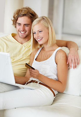 Buy stock photo A happy young couple doing their online banking from the comfort of their couch