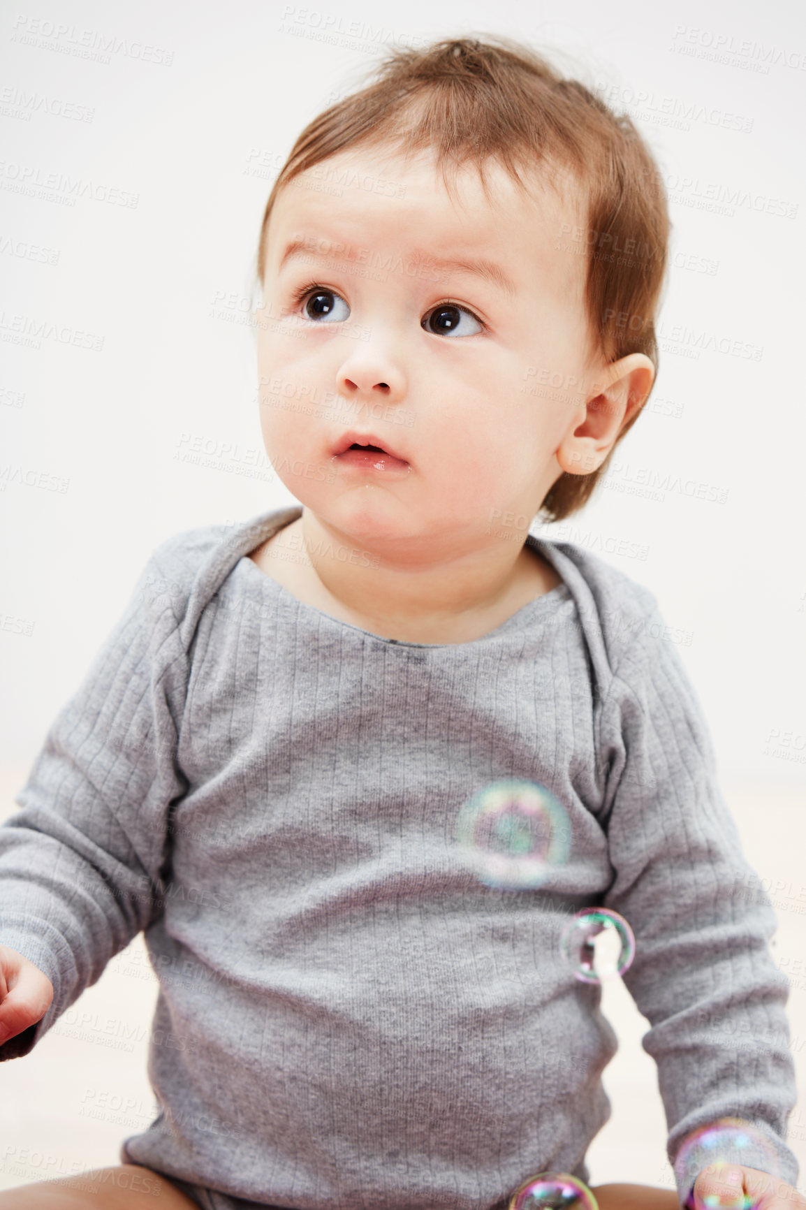 Buy stock photo Shot of an adorable baby boy looking at  bubbles floating in the air around him