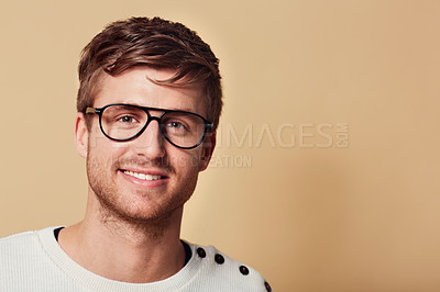 Buy stock photo Portrait, smile and glasses with a man on space in studio for eyewear marketing on a tan background. Face, vision and a happy young geek or nerd on mockup for optometry advertising and information