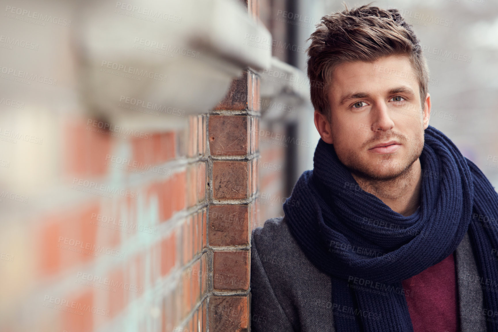 Buy stock photo Portrait, fashion and a young man in the city during winter for masculine style while leaning on a wall. Face, trendy and serious with a confident young person in an urban town to wear a warm scarf