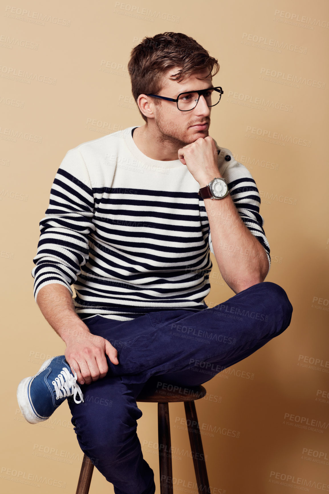 Buy stock photo Thinking, fashion and glasses with a man on a chair in studio on a tan background for vision or contemplation. Future, idea and pose with a confident young person sitting on stool feeling thoughtful