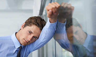 Buy stock photo A tired young businessman leaning against a glass wall