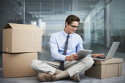 Buy stock photo A young businessman sitting on the floor working on a laptop and tablet while surrounded by boxes