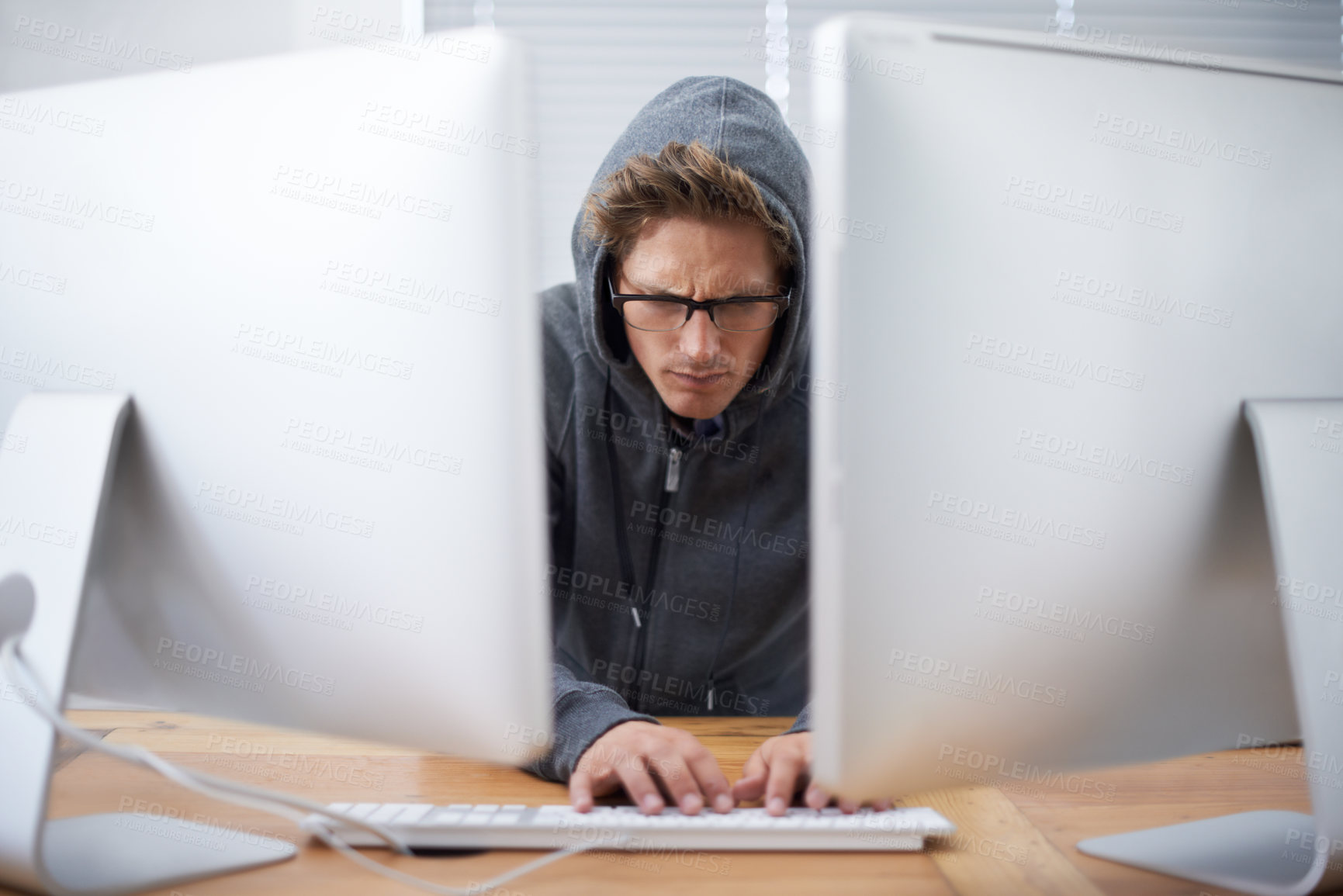 Buy stock photo A young hacker working on dual screens and a laptop wearing a hoodie