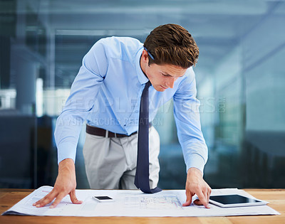 Buy stock photo A young architect examining his blueprints in his office while at his desk