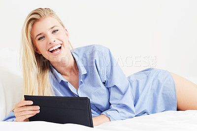 Buy stock photo A beautiful young blonde woman lying in bed with her digital tablet