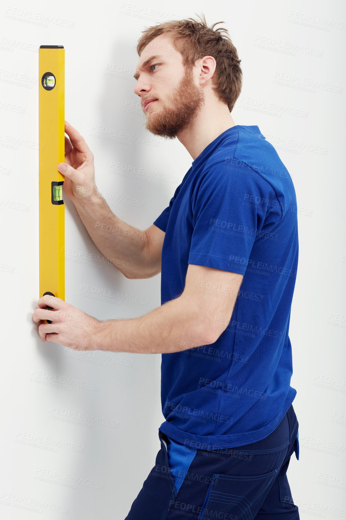 Buy stock photo An unshaven young man using a level to make sure the wall is straight