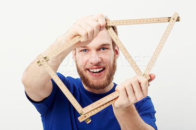 Buy stock photo Portrait of a happy young man holding up a carpenter's ruler in the shape of a house