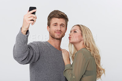 Buy stock photo Selfie, happy and young couple in a studio for memory with love, care and sweet relationship. Smile, kiss and man and woman with picture photography for positive and good attitude by white background
