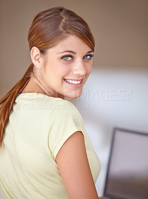 Buy stock photo A beautiful young woman glancing at you over her shoulder while using her laptop