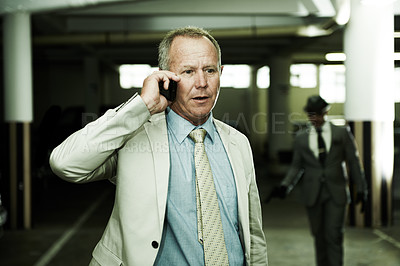 Buy stock photo An oblivious businessman talking on his cellphone as an armed assailant approaches from the shadows in a parkade