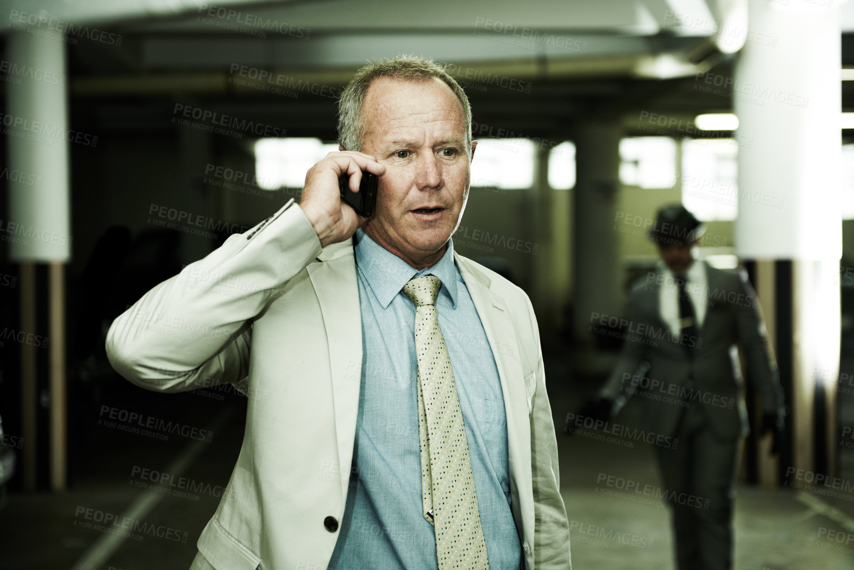 Buy stock photo An oblivious businessman talking on his cellphone as an armed assailant approaches from the shadows in a parkade