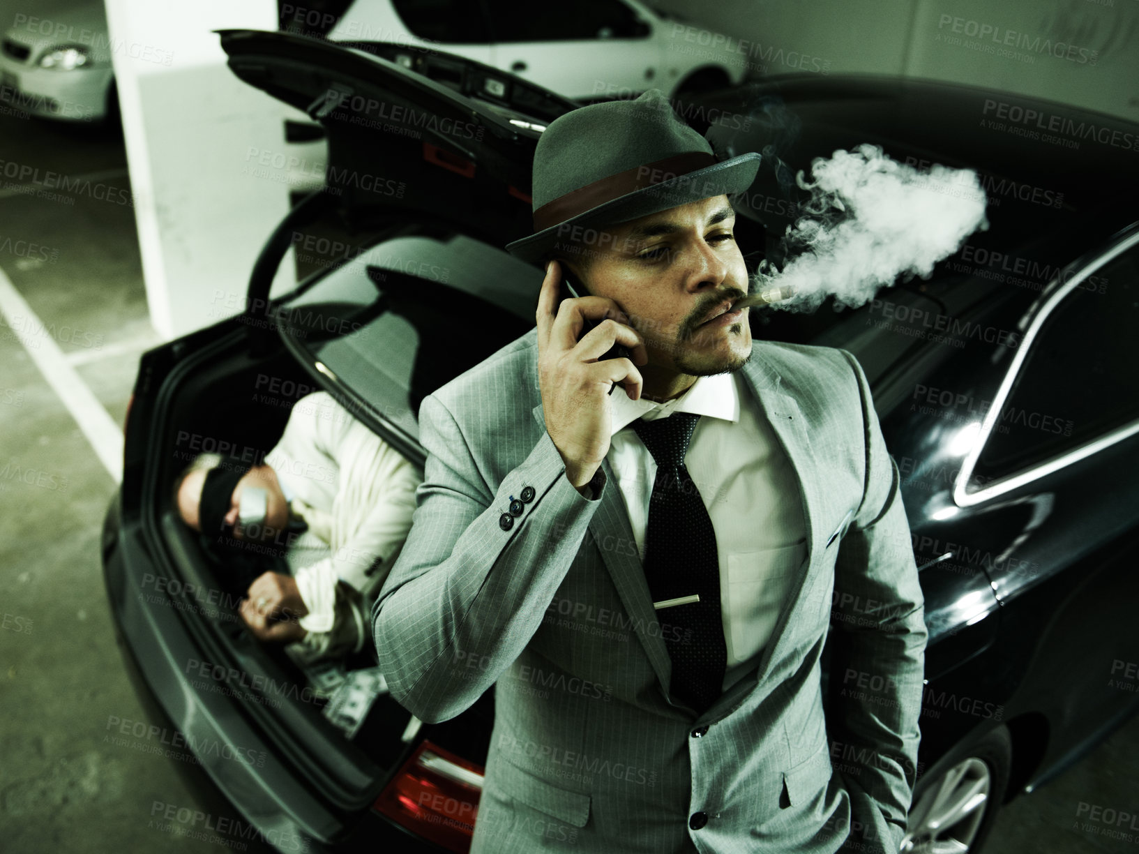 Buy stock photo Phone call, car and man with abduction in trunk for negotiation, kidnapping ransom and crime. Mafia, gangster criminal and person smoking in boot for terrorism, danger and robbery in parking lot