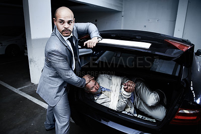 Buy stock photo A gangster stuffing a bound and gagged businessman into the boot of his car