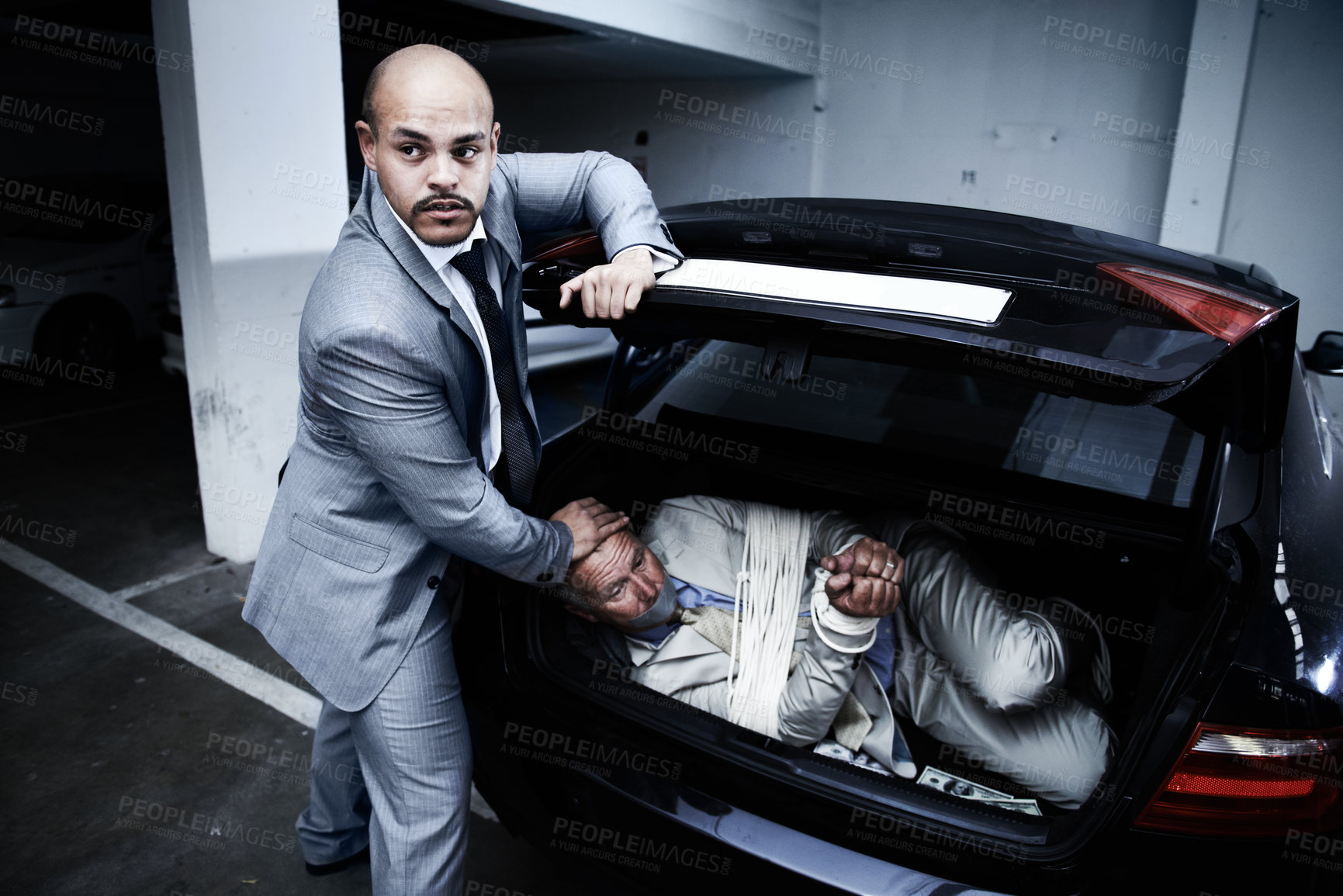 Buy stock photo A gangster stuffing a bound and gagged businessman into the boot of his car