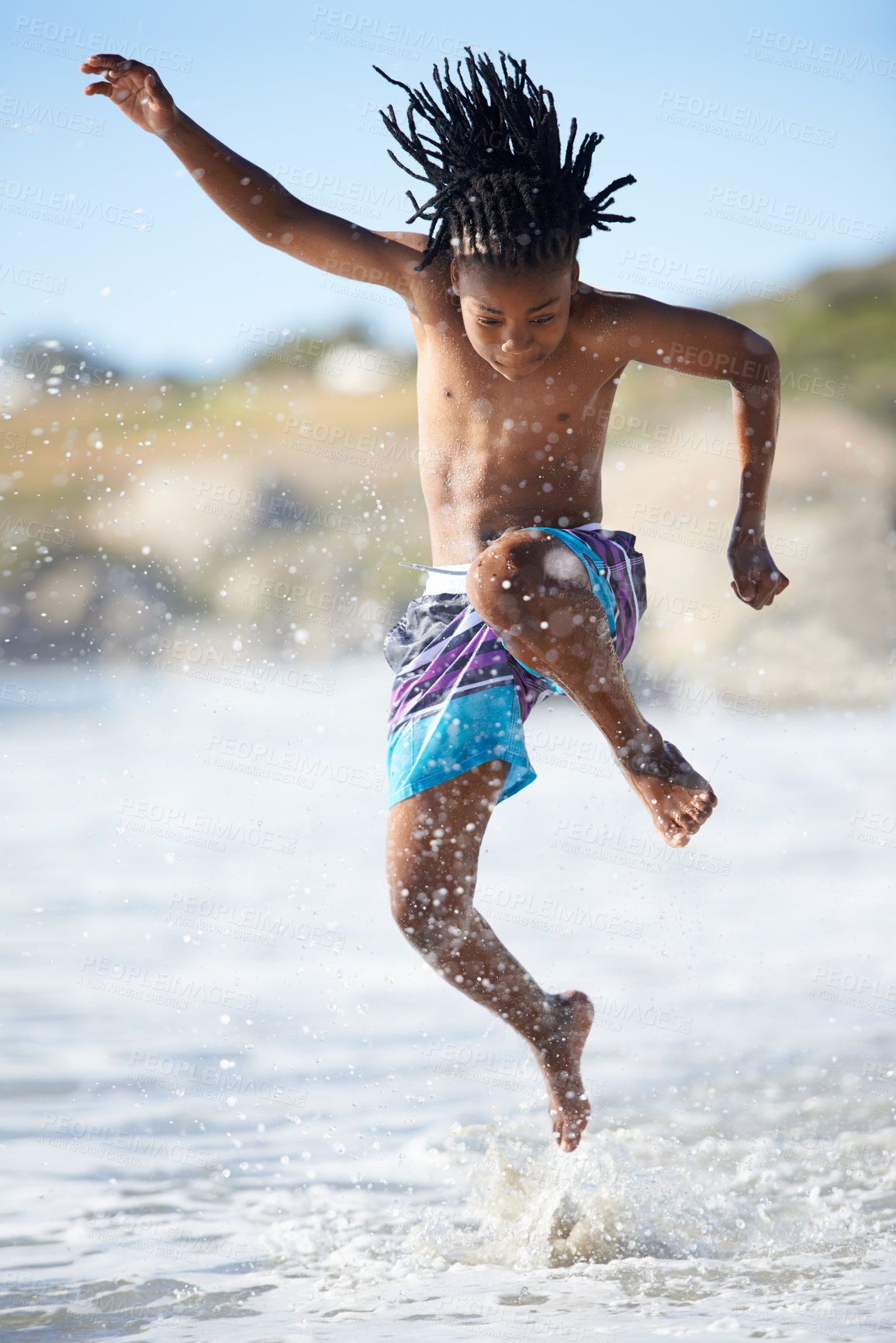 Buy stock photo An excited young boy leaping into the air while at the beach