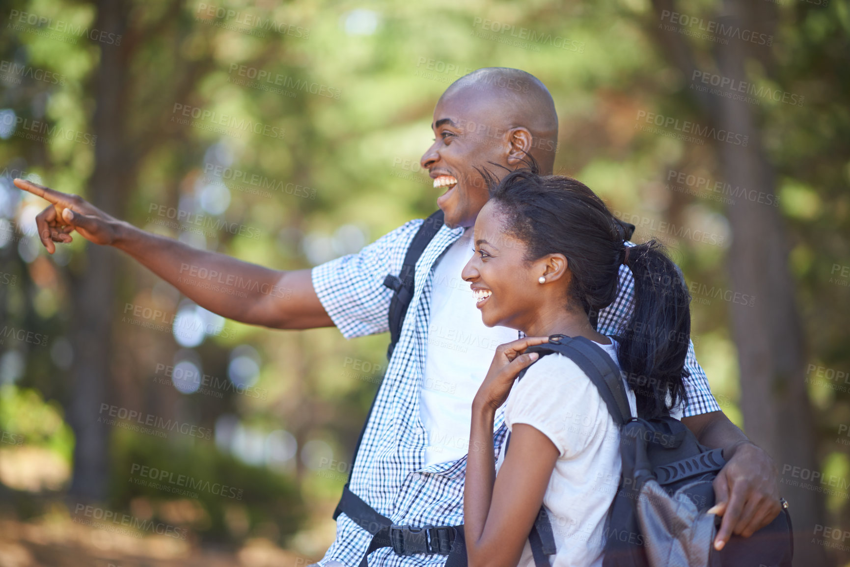 Buy stock photo Happy, pointing or black couple hiking in forest to relax or bond on holiday together in nature. Hug, speaking or African woman talking with joke, smile or man in woods trekking on outdoor adventure