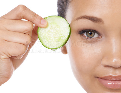 Buy stock photo Skincare, cucumber and woman face or eye beauty for cosmetics, natural product and Vitamin C makeup in studio. Portrait of a young, happy model with green fruit and dermatology on a white background