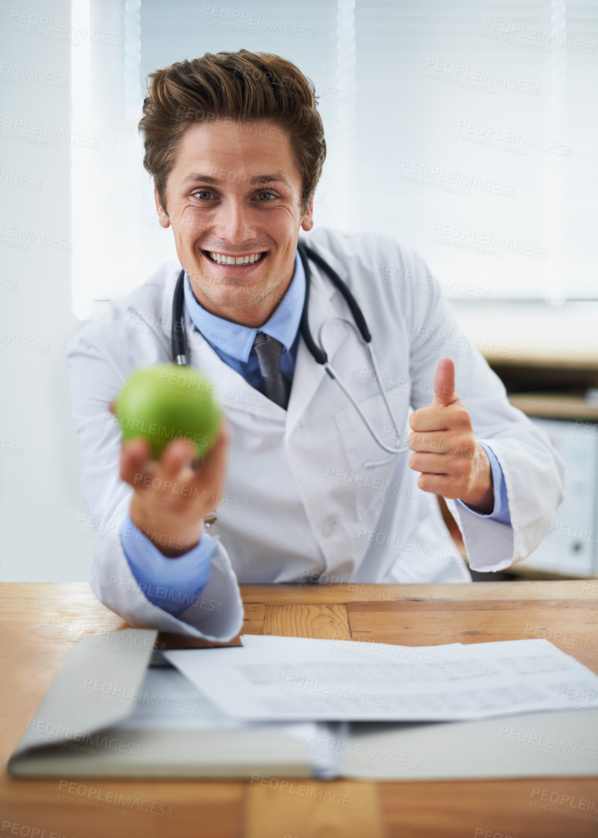Buy stock photo Thumbs up, apple and portrait of man doctor with stethoscope for positive, good and confident attitude. Happy, smile and young healthcare worker with fruit in medical office of hospital or clinic.