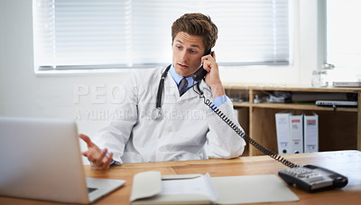 Buy stock photo Shot of a young doctor sitting in his office and talking on the phone