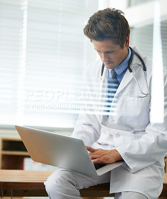 Buy stock photo Through the window shot of a young doctor working on a laptop
