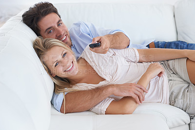 Buy stock photo A smiling couple lying on a sofa in a living room and cuddling while watching television