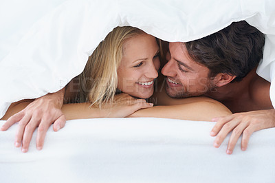 Buy stock photo A couple lying under a duvet cover and cuddling affectionately while looking into each others eyes