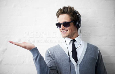 Buy stock photo A trendy young man holding out his palm while listening to music on his headphones