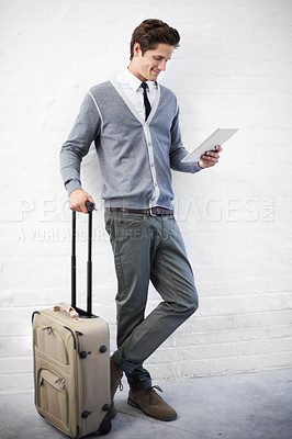 Buy stock photo A handsome young nerd with luggage working on his tablet